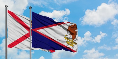 Jersey and American Samoa flag waving in the wind against white cloudy blue sky together. Diplomacy...