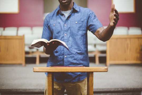 Closeup shot of a male reading the bible near a wooden stand with a blurred background