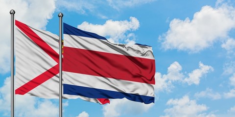 Jersey and Costa Rica flag waving in the wind against white cloudy blue sky together. Diplomacy concept, international relations.