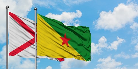 Jersey and French Guiana flag waving in the wind against white cloudy blue sky together. Diplomacy concept, international relations.