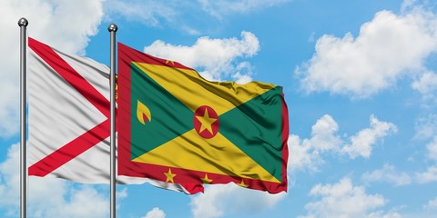 Jersey and Grenada flag waving in the wind against white cloudy blue sky together. Diplomacy concept, international relations.