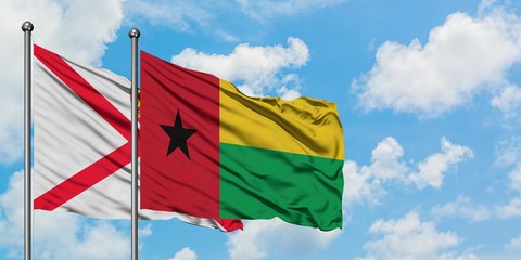 Jersey and Guinea Bissau flag waving in the wind against white cloudy blue sky together. Diplomacy concept, international relations.