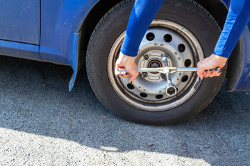 Beautiful girl with the cylinder key changes the wheel in the broken car. Replacement tires on the side of the country road. Car insurance concept