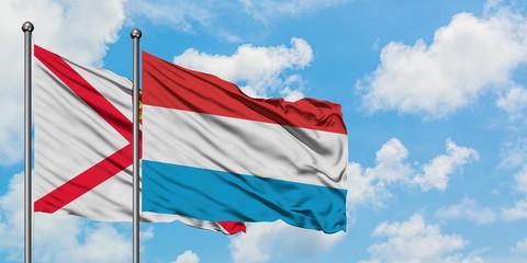 Jersey and Luxembourg flag waving in the wind against white cloudy blue sky together. Diplomacy concept, international relations.