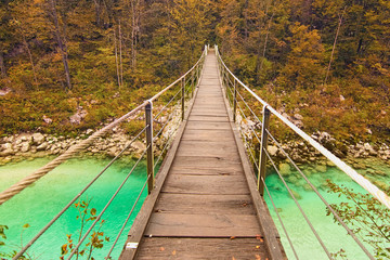 Wide angle landscape view of spectacular suspended wooden bridge over alpine Soca River. Autumn colored trees in the background. Concept of landscape and nature. National Park of Triglav, Slovenia