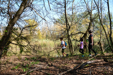 Side view of happy family walking in a wood by the lake. Cheerful single mother with her son and daughter walking in a national park by the lake. Horizontal