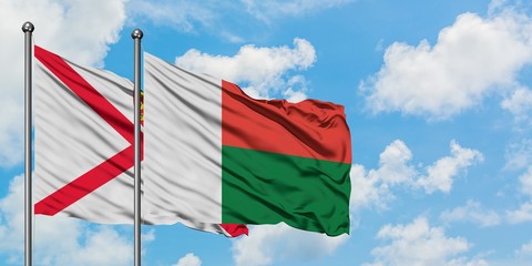 Jersey and Madagascar flag waving in the wind against white cloudy blue sky together. Diplomacy concept, international relations.