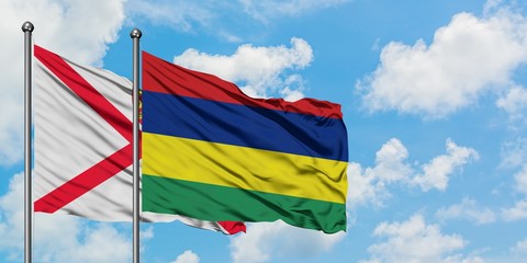 Jersey and Mauritius flag waving in the wind against white cloudy blue sky together. Diplomacy concept, international relations.
