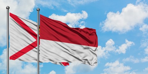 Jersey and Monaco flag waving in the wind against white cloudy blue sky together. Diplomacy concept, international relations.