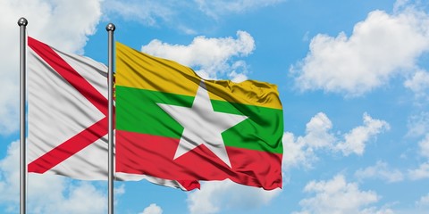 Jersey and Myanmar flag waving in the wind against white cloudy blue sky together. Diplomacy concept, international relations.