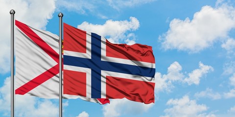 Jersey and Norway flag waving in the wind against white cloudy blue sky together. Diplomacy concept, international relations.