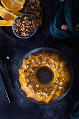 Bundt cake, orange cake with walnuts and yellow sugar icing with turmeric spice. Dark background. View from above