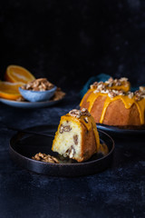 Bundt cake, orange cake with walnuts and yellow sugar icing with turmeric spice. Dark background. With a cut piece