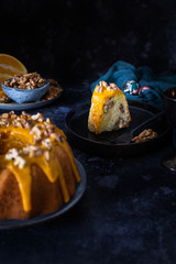 Bundt cake, orange cake with walnuts and yellow sugar icing with turmeric spice. Dark background. With a cut piece