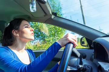 Angry woman driving a car. The girl with an expression of displeasure is actively gesticulating behind the wheel of the car. Car insurance concept