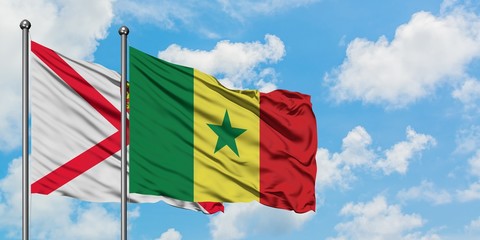 Jersey and Senegal flag waving in the wind against white cloudy blue sky together. Diplomacy concept, international relations.