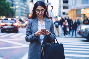Joyful young female using smartphone on crosswalk