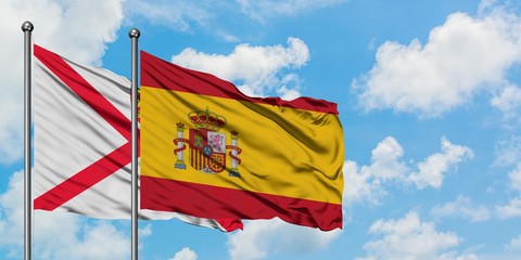 Jersey and Spain flag waving in the wind against white cloudy blue sky together. Diplomacy concept, international relations.