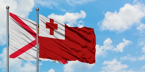 Jersey and Tonga flag waving in the wind against white cloudy blue sky together. Diplomacy concept, international relations.