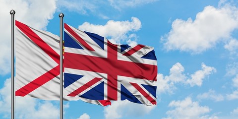 Jersey and United Kingdom flag waving in the wind against white cloudy blue sky together. Diplomacy concept, international relations.