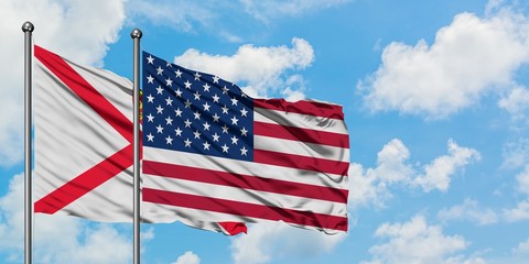 Jersey and United States flag waving in the wind against white cloudy blue sky together. Diplomacy concept, international relations.