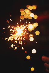 New Year, a burning sparkler in hand with bright bokeh on a dark background