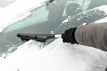 Woman cleaning car from the snow with brush. People in snowy cold weather in winter and...