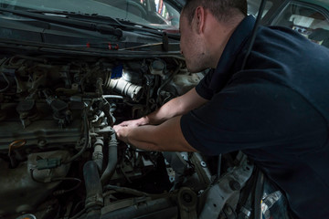 Naklejka na ściany i meble Auto mechanic working on car engine in mechanics garage. Car repair service.