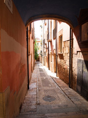 View from the arch to the narrow street with stone pavement and decorated with mosaics, Tarragona.