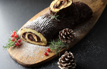 Tronchetto di Natale al cioccolato, Buche de Noel sul tagliere di legno. Decorazioni natalizie su sfondo scuro. Vista da vicino