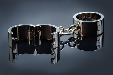 Gold handcuffs lie on a gray metal mirror surface