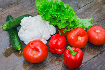 Fresh vegetables cauliflower cucumbers salad tomatoes red bell pepper covered with raindrops on the background of a wooden table.