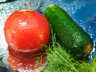 Tomato and dill and cucumber in drops against a blue mirror background. Ingredients for a summer salad.