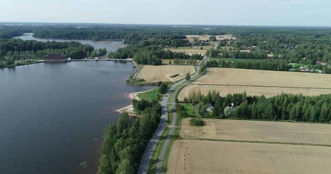 Flying over the Dam on the river. Strong current. Green fields and forest. Summer, cloudy sky. Top view. Aerial footage.