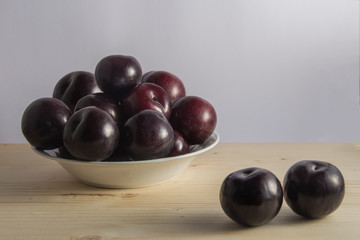 Still life with a bowl with plums and three loose on wooden background