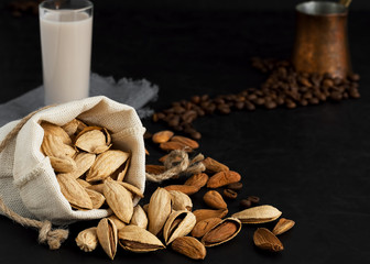 Almond milk with almonds on a black background. Coffee beans and espresso cezve. Close-up. Healthy eating concept. Copy space Natural light.