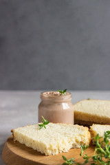 Fresh homemade chicken liver pate on bread with thyme on a wooden cutting board. 
