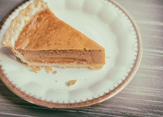 Close up view of a piece of pumpkin pie with crumbs on a white plate. 