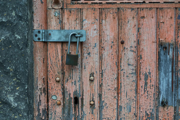 Fragment of an old wooden door locked with a padlock. The pink paint on the door cracked and cracked. There is a hole for the key to the mortise lock. Background. Texture.