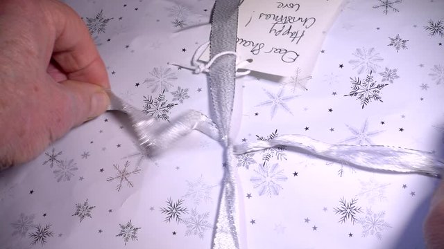 Slow motion close POV overhead shot of a man&rsquo;s hands undoing the ribbon bow from the wrapping around a Christmas present.