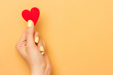 Female hands hold a wooden heart symbol. Bright manicure. Warm yellow background