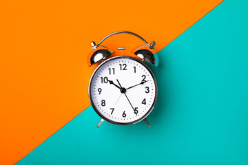 Retro alarm clock on half orange and yellow background - obrazy, fototapety, plakaty