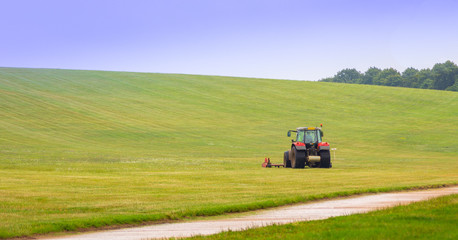 Tractor mower on a green field with blue sky