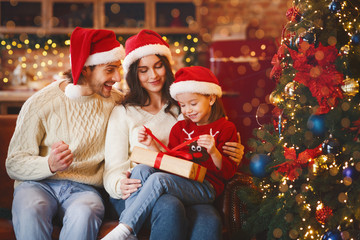 Obraz na płótnie Canvas Cute festive girl openng xmas gifts with mom and dad