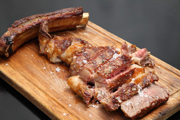Medium-roasted steak cut into pieces on a wooden board with sauce and seasonings. Delicious steak. Beef steak medium rare on vegetable cushion. Beef steak on wooden plate. 