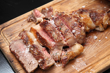 Medium-roasted steak cut into pieces on a wooden board with sauce and seasonings. Delicious steak. Beef steak medium rare on vegetable cushion. Beef steak on wooden plate. 