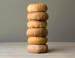 Tall stack of a half dozen glazed cake doughnuts on a wood table, gray background. 
