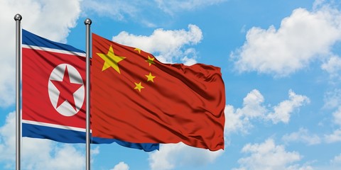 North Korea and China flag waving in the wind against white cloudy blue sky together. Diplomacy concept, international relations.