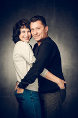 Playful mature married couple photographed in the studio. Handsome man in jeans and smiling woman in shirt playing