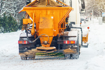 Municipal car sprinkles snowy roads with sand and salt. Snow blower. Winter anti-slip road handling concept